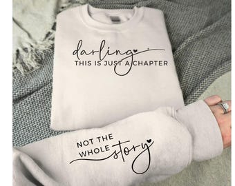Może przedstawiać: Biała bluza z napisem "darling, this is just a chapter, not the whole story" w czarnym, ozdobnym pismie z małym symbolem serca po każdym zdaniu.