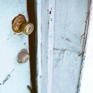 May include: A close-up of a weathered, light blue wooden door with a brass doorknob and keyhole. The door is slightly ajar, revealing a sliver of the interior.