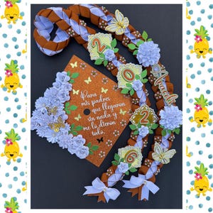May include: A graduation lei and cap set. The lei is brown and white braided ribbon with floral and butterfly accents. The cap is orange with text and butterfly decorations. The text on the cap reads "Para mis padres que llegaron sin nada y me lo dieron todo."