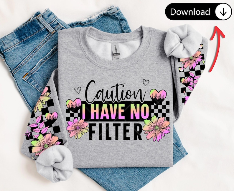 May include: A gray sweatshirt with the text "Caution I Have No Filter" in black and neon colors. The sleeves feature a checkered pattern with flowers and hearts in pink, yellow, and black. The sweatshirt is folded on top of blue jeans.