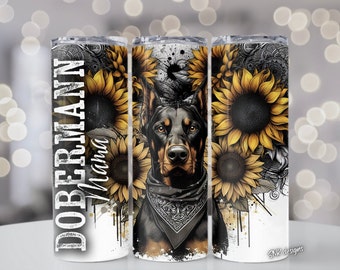 Op de afbeelding: Een witte tumbler met een zwart-witte Dobermann Pinscher hond die een bandana draagt en zonnebloemen. De tekst "Doberman Mama" staat aan de linkerkant van de tumbler.