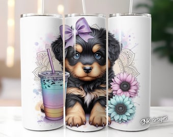 May include: A white tumbler with a black and brown puppy wearing a purple bow. The puppy is surrounded by watercolor flowers and a mandala design. The tumbler has a clear lid and a straw.