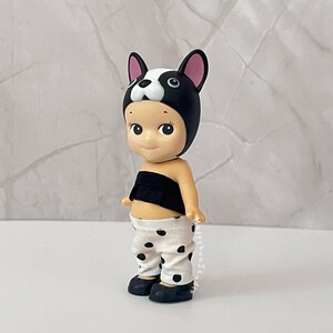 K&ouml;nnte beinhalten: Eine kleine Figur mit einer schwarz-wei&szlig;en Franz&ouml;sische Bulldogge-Kopfbedeckung, einem schwarzen tr&auml;gerlosen Oberteil und einer wei&szlig;en Hose mit schwarzen Punkten. Die Figur hat einen hellen Hautton, rosige Wangen und schwarze Schuhe.