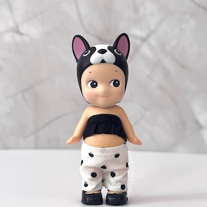 K&ouml;nnte beinhalten: Eine kleine Figur mit einer schwarz-wei&szlig;en Franz&ouml;sische Bulldogge-M&uuml;tze, einem schwarzen, ger&uuml;schten Schlauchoberteil und einer wei&szlig;en Hose mit schwarzen Punkten. Die Figur hat helle Haut, gro&szlig;e dunkle Augen und tr&auml;gt kleine schwarze Schuhe.