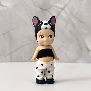 K&ouml;nnte beinhalten: Eine kleine Figur mit einer schwarz-wei&szlig;en Franz&ouml;sische Bulldogge-Kopfbedeckung, einem schwarzen tr&auml;gerlosen Oberteil und einer wei&szlig;en Hose mit schwarzen Punkten. Die Figur hat helle Haut, gro&szlig;e dunkle Augen und tr&auml;gt kleine schwarze Schuhe.