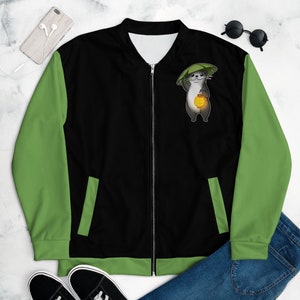 May include: A black and green bomber jacket featuring a cartoon otter holding a lantern and wearing a leaf hat. The jacket has a zip fastening and two pockets.