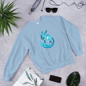 May include: A light blue sweatshirt with a graphic of a blue and white creature with red eyes. The creature is curled up with its tail wrapped around its body.