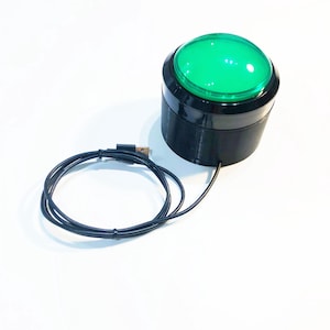 Könnte beinhalten: Ein runder Knopf in Schwarz und Grün mit einem USB-Kabel. Der Knopf leuchtet grün.