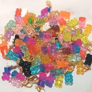 May include: A collection of colorful gummy bear charms in various colors, including orange, yellow, green, blue, pink, and purple. Each charm is attached to a gold-colored clasp, suitable for jewelry or craft projects.