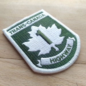 Puede incluir: Parche bordado verde y blanco con el texto "Trans-Canada Highway" y una hoja de arce blanca con el número "1" en su interior.