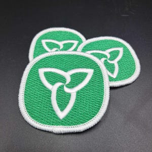 May include: Three green and white embroidered patches with a stylized three-leaf clover design. The patches are round with a white border and a green background. The clover design is white.