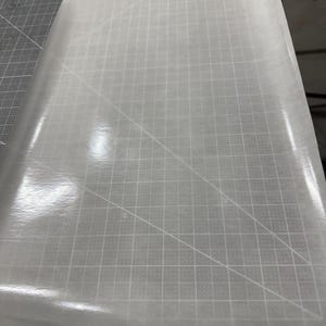 May include: A white sheet of parchment paper with a grid pattern on a gray cutting mat.