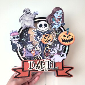 Puede incluir: Un adorno para pastel con personajes de la pel&iacute;cula Pesadilla antes de Navidad. El adorno incluye a Jack Skellington, Sally, Oogie Boogie, Zero y el Rey Calabaza. El adorno est&aacute; decorado con purpurina y tiene una pancarta que dice "DANIEL".