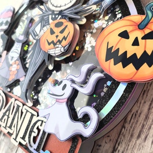 Puede incluir: Un adorno para pastel en blanco y negro con personajes de la pel&iacute;cula Pesadilla antes de Navidad. El adorno incluye a Jack Skellington, Sally, Zero el perro fantasma y una calabaza. El adorno est&aacute; decorado con purpurina y tiene el nombre "Daniel" escrito en &eacute;l.