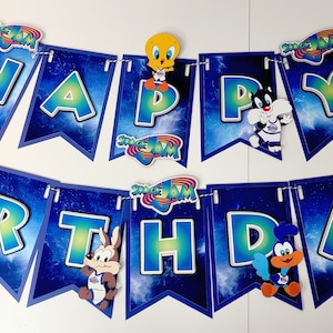 May include: A blue and green "Happy Birthday" banner with a space jam theme. The banner features characters from the movie Space Jam, including Bugs Bunny, Tweety Bird, and Daffy Duck. Each letter is decorated with a different character.