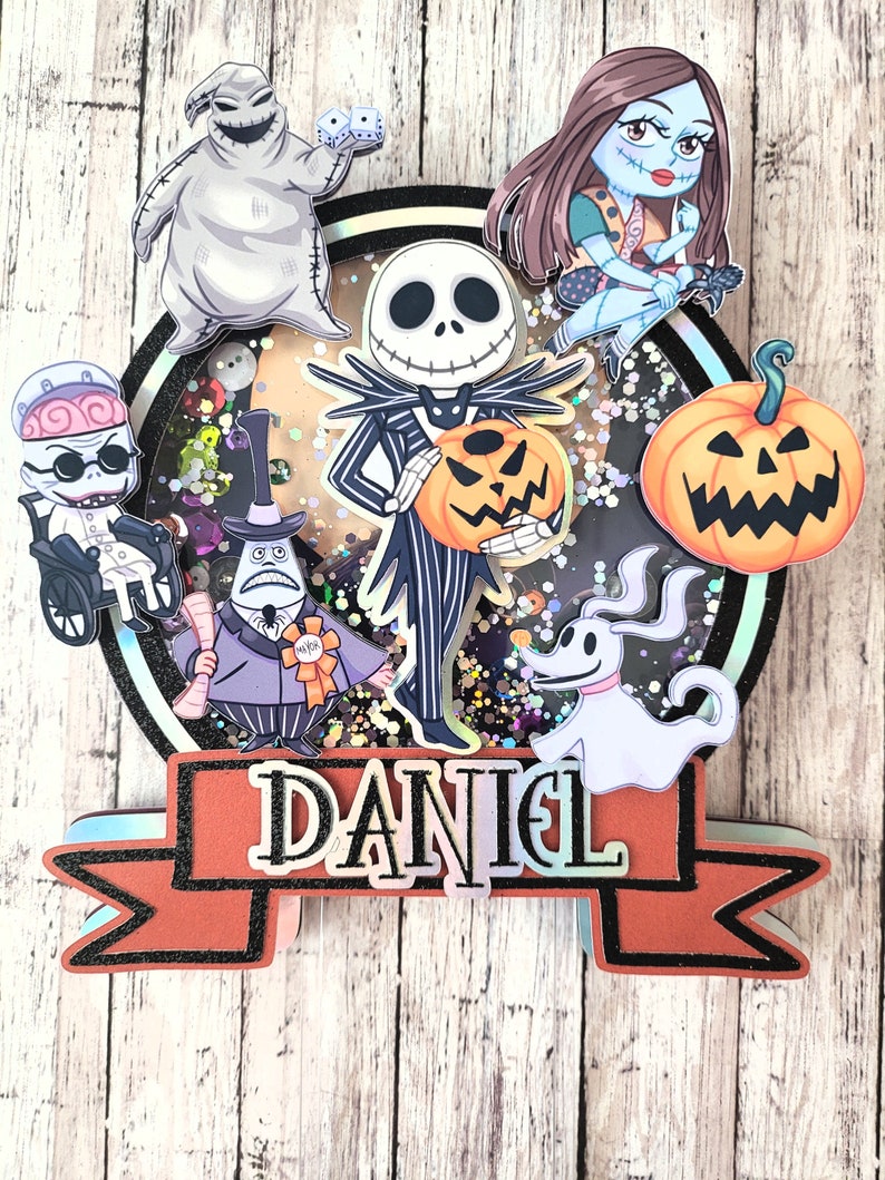 Puede incluir: Un adorno redondo para pastel con un fondo brillante que presenta personajes de Pesadilla Antes de Navidad. Los personajes incluyen a Jack Skellington, Sally, Zero, Oogie Boogie y el Rey Calabaza. El adorno tiene una pancarta con el nombre "DANIEL" en ella.