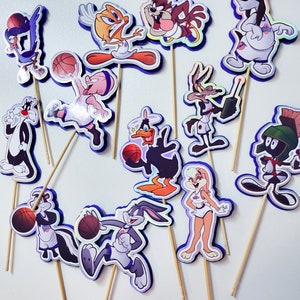 May include: A set of 13 cartoon character cake toppers featuring characters from the Looney Tunes franchise. The characters are all wearing basketball uniforms and holding basketballs. The toppers are printed on cardstock and have a glossy finish.