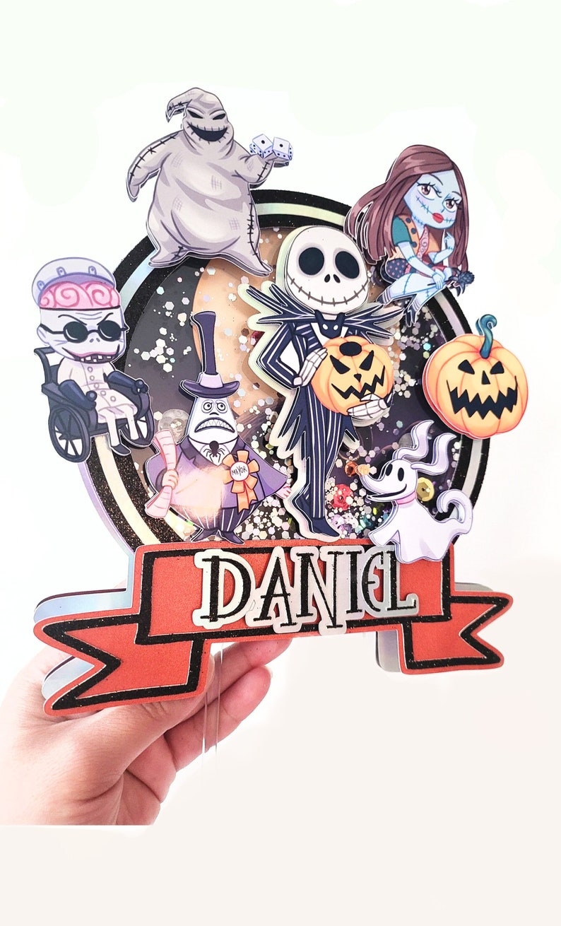 Puede incluir: Una pancarta roja y negra con el nombre "DANIEL" en letras blancas. La pancarta est&aacute; decorada con purpurina y tiene un contorno negro. La pancarta est&aacute; rodeada de personajes de Pesadilla antes de Navidad, incluyendo a Jack Skellington, Sally, Oogie Boogie y Zero.