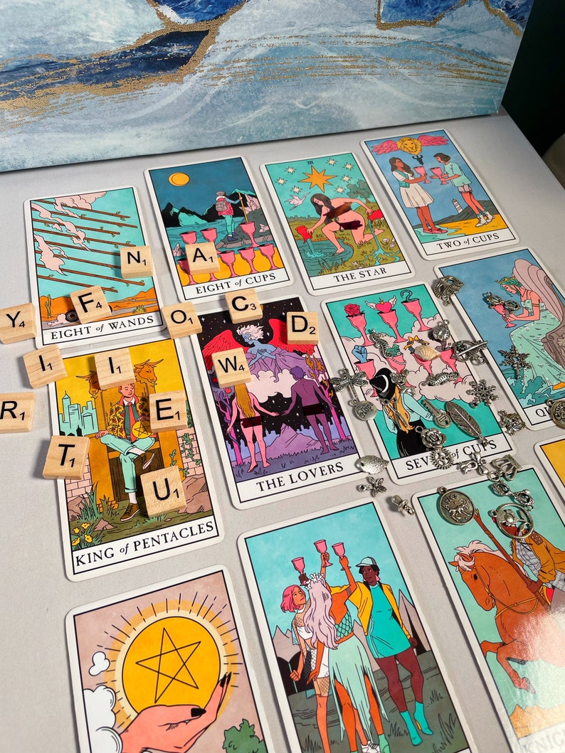 Pode incluir: Cartas de tar&ocirc; espalhadas sobre uma superf&iacute;cie branca com pe&ccedil;as de letras de madeira que soletram palavras como "Oito de Varinhas", "Rei de Pent&aacute;culos", "Os Amantes" e "Sete de Copas".