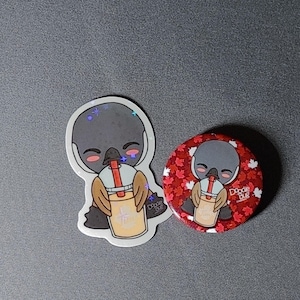 Puede incluir: Una pegatina y un botón con un pájaro de dibujos animados bebiendo una bebida con una pajita. La pegatina tiene un acabado holográfico. El botón tiene un fondo rojo con formas de hojas blancas y el texto "Doodle Bug".