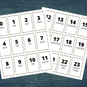 May include: A set of 24 white cards with black numbers and words, from zero to twenty-three. Each card has a rainbow border.