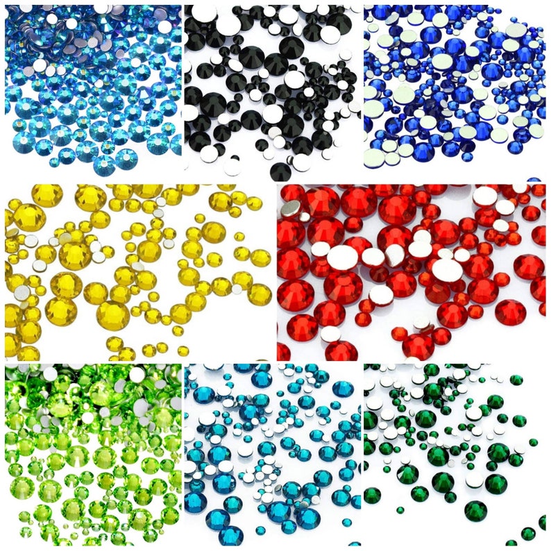 May include: Assortment of colorful rhinestones in various colors, including blue, black, yellow, red, green, and turquoise. The rhinestones are scattered on a white background.