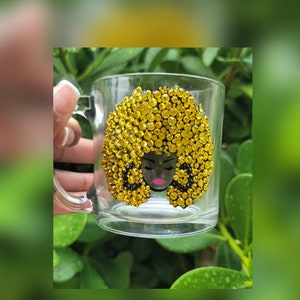 May include: A clear glass mug with a black and pink silhouette of a woman with a large, yellow, rhinestone afro.