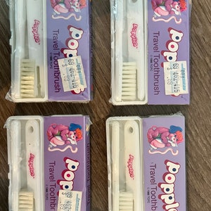 Puede incluir: Cuatro juegos de cepillos de dientes de viaje de color morado y rosa con el personaje Popples. Cada juego incluye un cepillo de dientes y un estuche de viaje. La etiqueta de precio dice "$0.89".