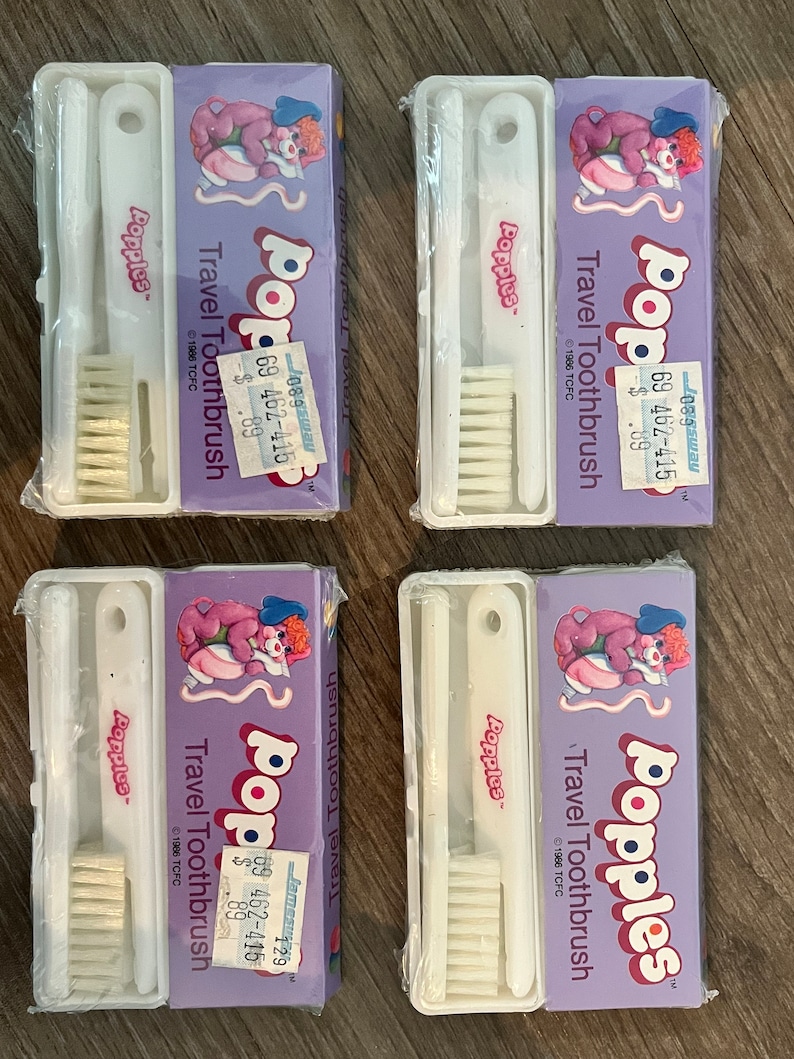 Puede incluir: Cuatro juegos de cepillos de dientes de viaje de color morado y rosa con el personaje Popples. Cada juego incluye un cepillo de dientes y un estuche de viaje. La etiqueta de precio dice "$0.89".