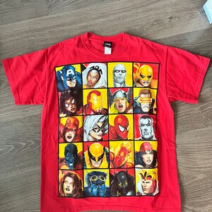 May include: Red t-shirt with a graphic print of various Marvel Comics superheroes, including Captain America, Iron Man, Spider-Man, Wolverine, and more.