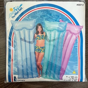 May include: The Wet Set inflatable pool floats in blue, teal, and purple. The package shows a woman in a swimsuit standing next to the floats. The floats measure approximately 183 cm x 76 cm (72" x 30").