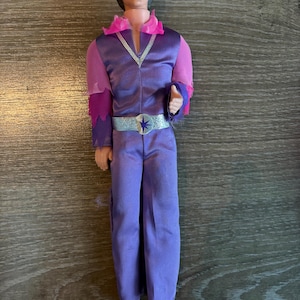 May include: A set of three ceramic mugs with a speckled, matte finish. The mugs are in shades of cream, light brown, and dark brown. Each mug has a simple, minimalist design and a rounded handle.