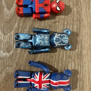 May include: Three collectible figurines: a red and blue Spiderman, a blue bear with white flame designs, and a blue bear with a Union Jack design.