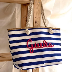 borsa a righe bianca e blu con manici di corda e scritta in rilievo del nome color fucsia