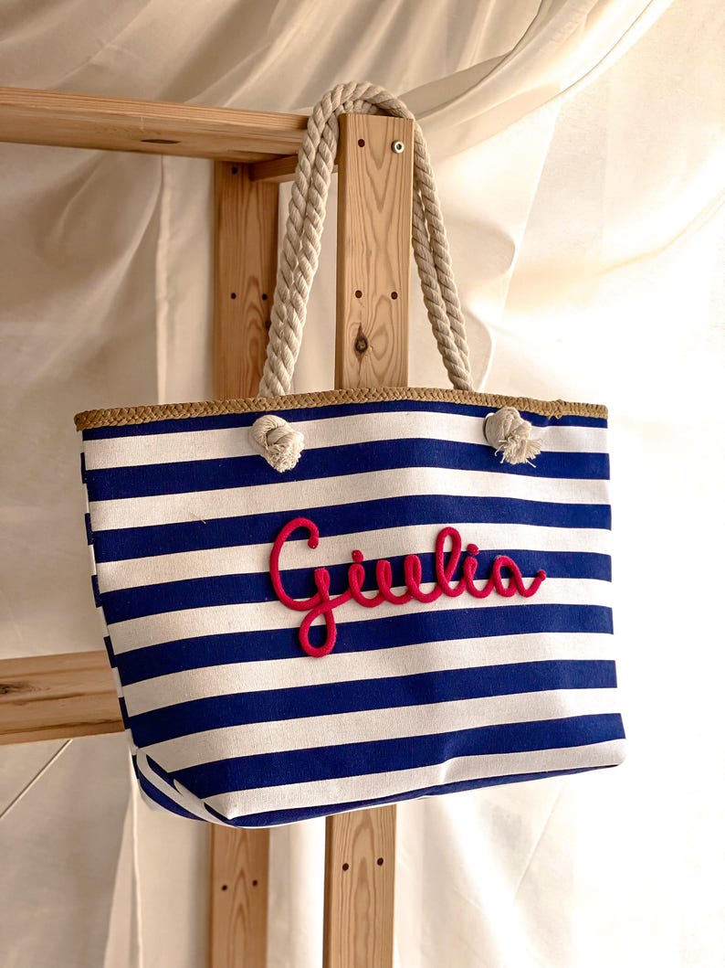 borsa a righe bianca e blu con manici di corda e scritta in rilievo del nome color fucsia