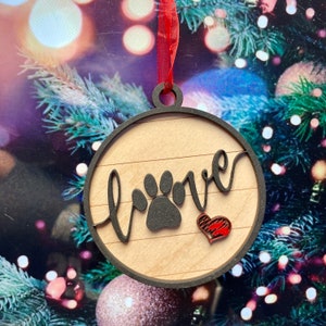 May include: A round wooden ornament with a black paw print and the word "love" written in cursive. A red heart is also on the ornament.
