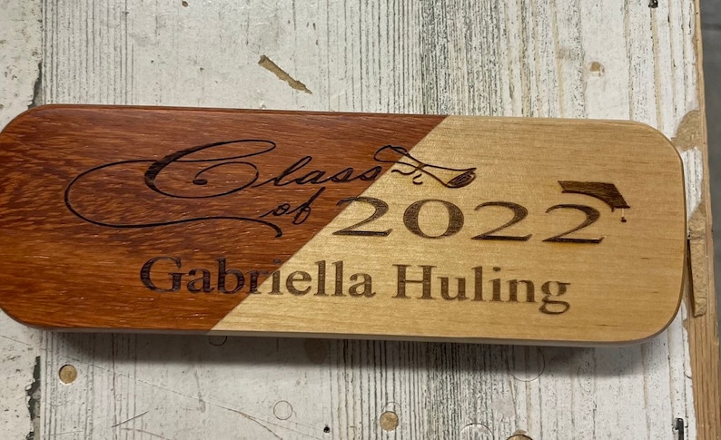 May include: A wooden plaque with a brown and light wood finish. The plaque is engraved with the text "Class of 2022" and "Gabriella Huling".