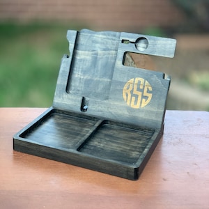 May include: A black wooden phone stand with a tray for keys and other small items. The stand has a slot for a phone and a watch holder. The stand is personalized with the initials "RSS" in gold.