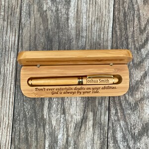 May include: A wooden pen box with a gold pen inside. The box is engraved with the text "Joshua Smith" and the quote "Don't ever entertain doubts on your abilities. God is always by your side."