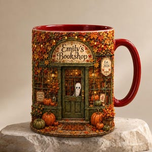 May include: A ceramic mug with a red interior and handle, featuring a detailed wrap-around illustration of a bookstore storefront named Emily's Bookshop. The design includes autumn leaves, pumpkins, a small ghost in the doorway, and text reading Est. 2026.