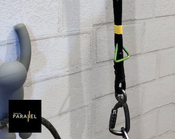 May include: A white plastic figure with arms raised, holding a black rope with a yellow stripe. The rope is attached to a green metal triangle and a silver carabiner.