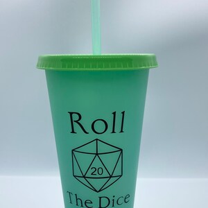 May include: A green and white tumbler with a green lid and straw. The tumbler has the words "Roll The Dice" and a 20-sided die graphic printed on it.