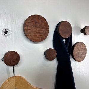 May include: Five round wooden wall hooks in various sizes, with a dark brown finish. A blue scarf is hanging on one of the larger hooks.