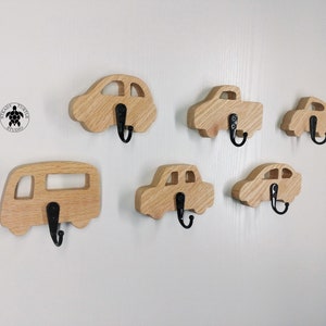 May include: Six wooden car-shaped hooks with black metal hooks. The hooks are mounted on a white wall.