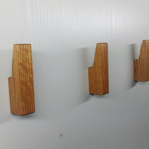 May include: Three wooden wall hooks in varying sizes. The hooks are made of light brown wood and have a simple, modern design. They are mounted on a white wall, offering a minimalist aesthetic for organizing coats, bags, or other items.
