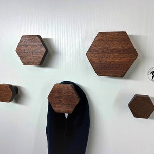 May include: Five wooden hexagonal hooks mounted on a white wall. The hooks are of varying sizes and are made from dark brown wood. The hooks are ideal for hanging coats, hats, or other items.
