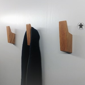Peut inclure: Trois crochets muraux en bois de couleur brun clair. Les crochets sont inclinés et ont un design moderne. Une écharpe bleu foncé est accrochée à l'un des crochets.