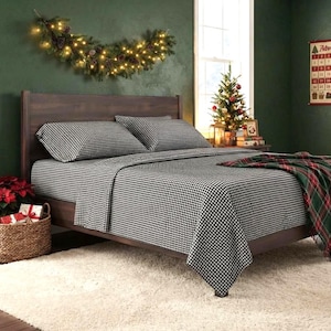 May include: A bed featuring a dark wood headboard and frame, dressed in black and white gingham patterned sheets and two matching pillowcases. A green, red, and white plaid throw blanket is draped over the corner of the bed.