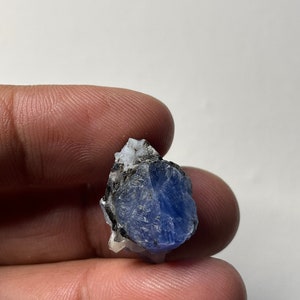 May include: A rough, blue sapphire crystal with a white matrix. The crystal is about 1 inch in size.