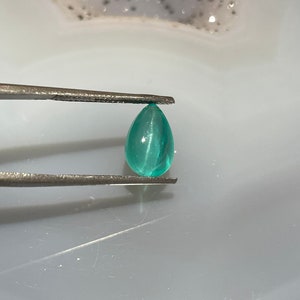 Op de afbeelding: Een traanvormige groene edelsteen vastgehouden door een pincet. De edelsteen heeft een glad, gepolijst oppervlak en een lichtgroene kleur.